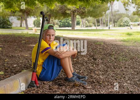 Teenager in zwangloser Kleidung sitzt im Park auf einem Roller entspannender, aktiver Lebensstil eines Kindes Stockfoto