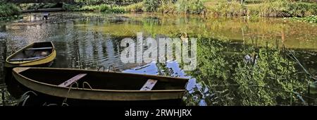 2 alte hölzerne Ruderboote liegen auf dem Wasser am Ufer eines ruhigen idyllischen Sees. Bäume aus grünem Sommerwald spiegeln sich auf glatter Oberfläche wider. Ruhig ruhig und entspannend Stockfoto