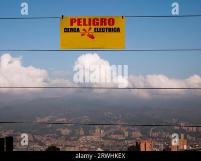 Gelbes Warnschild auf spanisch, das an einem elektrischen Zaun hängt, mit der Skyline einer Stadt im Hintergrund Stockfoto