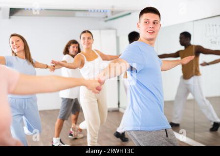 Aufgeregte junge Männer und Frauen mittleren Alters, Paare, die sich zur Seite drehen, während sie im Studio für Erwachsene tanzen Stockfoto