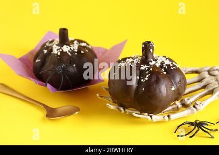 Köstliche Schokoladenkuchen, Skelett Hand und Löffel für Halloween Feier auf gelbem Hintergrund, Nahaufnahme Stockfoto