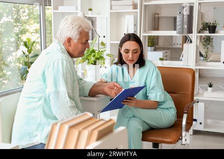 Ärztin, die dem leitenden Patienten in der Arztpraxis etwas auf dem Clipboard zeigt Stockfoto