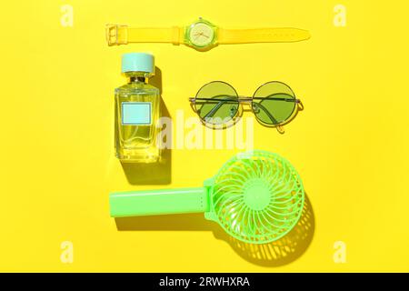 Komposition mit tragbarem Elektroventilator und stilvollem weiblichem Zubehör auf gelbem Hintergrund Stockfoto