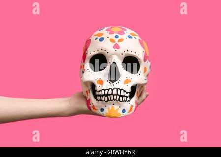 Weibliche Hand hält bemalten menschlichen Schädel für Mexikos Tag der Toten (El Dia de Muertos) auf rosa Hintergrund Stockfoto