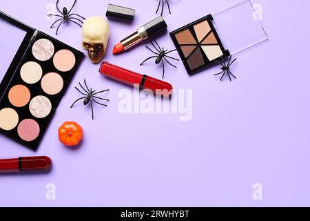 Lippenstifte und verschiedene dekorative Kosmetik mit Halloween-Dekor auf lila Hintergrund Stockfoto