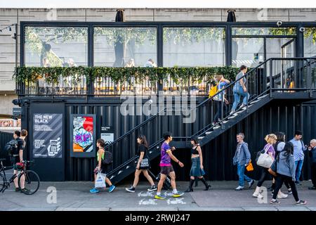 Leute, die an der Boxpark Pop Up Mall, Shoreditch, London, Großbritannien vorbeigehen. Stockfoto