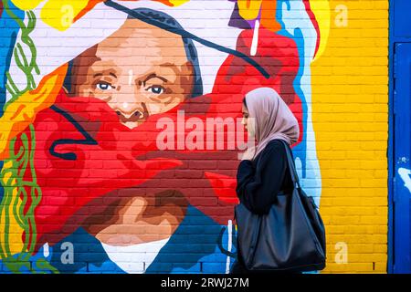 Eine junge Frau spaziert vorbei an farbenfroher Street Art, Shoreditch, London, UK. Stockfoto