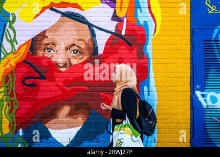 Eine junge Frau spaziert vorbei an farbenfroher Street Art, Shoreditch, London, UK. Stockfoto