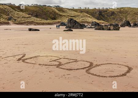 Durness, Schottland, Großbritannien - 4. Mai 2023 - NC500 geschrieben in den Sand am durness Beach gegenüber dem Strand Wohnmobile können auf der Klippe gesehen werden Stockfoto