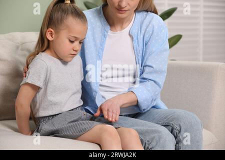 Mutter trägt Salbe auf das Knie ihrer Tochter auf der Couch auf Stockfoto