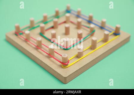 Geobord aus Holz mit Gummibändern auf grünem Hintergrund, Nahaufnahme. Lernspielzeug für die Entwicklung motorischer Fähigkeiten Stockfoto