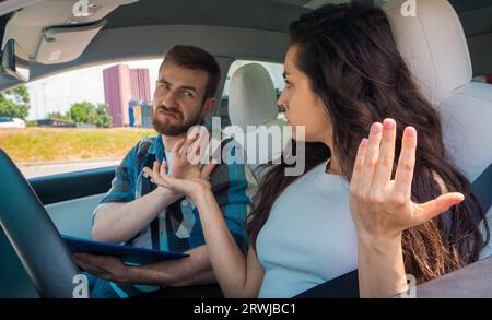 Junge Frau und männlicher Ausbilder sprechen Gesten mit Grimaken und sitzen im Auto während der Fahrprüfung. Fahrprüfung, Fahrerkurse, Prüfungskonzept Stockfoto