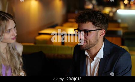 Glücklicher junger Mann in Gläsern, der mit seinen Freunden spricht, während er im Restaurant sitzt und sich ausruht. Lifestyle- und Freundschaftskonzept. Zeitlupe Stockfoto