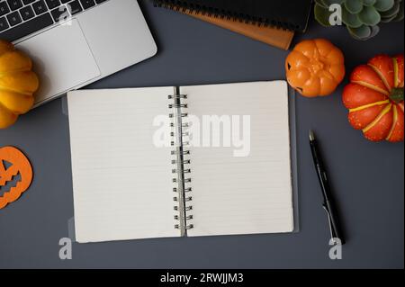 Ein Arbeitsbereich im Halloween-Stil mit einem geöffneten Buch oder Tagebuch, einem Stift, einem Laptop und Mini-Kürbissen für Halloween. Oberes Bild Stockfoto