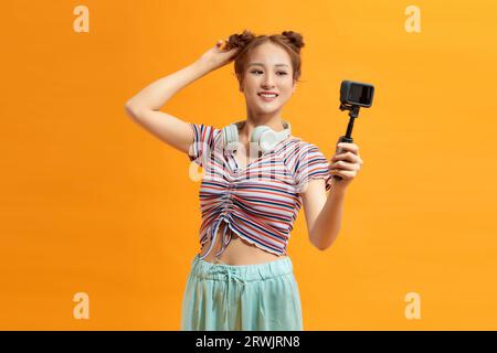 Junge Frau mit gelbem Hintergrund, die Fotos vor der Kamera macht Stockfoto