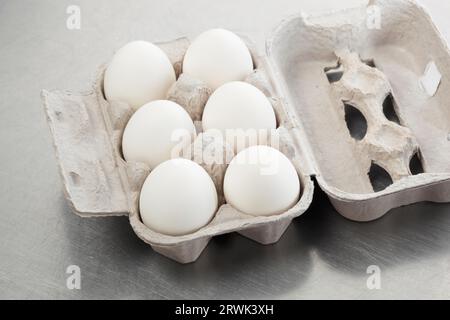 Sechs weiße Hühnereier in einem Karton auf einer zerkratzten Metalloberfläche Stockfoto