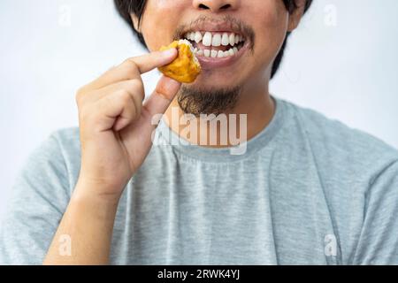 Mann, der gebratenen Tofu mit weißem Hintergrund isst. Traditionelles indonesisches Essen Stockfoto