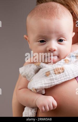 Zehn Wochen alten Babymädchen auf Mutters Schulter zeigen Zunge Stockfoto