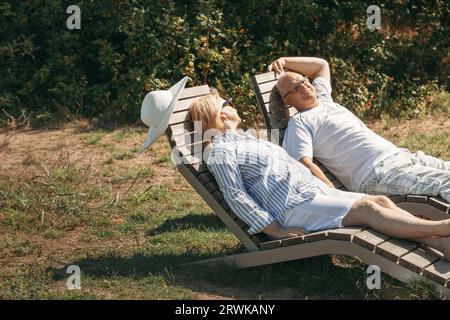 Ein paar süße ältere Leute liegen auf den Liegen und halten die Hände in der Sonne. Stockfoto