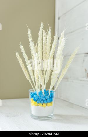 Weizenohren in blauer und gelber Vase. Getrocknete Pflanzen in ukrainischem Farbtopf. Weißer Weizen auf weißem Holzregal. Elegante Einrichtung mit Öko-Design. Müslistrauß. Stockfoto