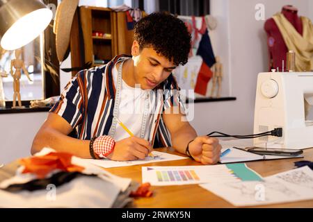 Konzentrierter birassischer Modedesigner, der Entwürfe skizziert und im Studio am Schreibtisch sitzt Stockfoto