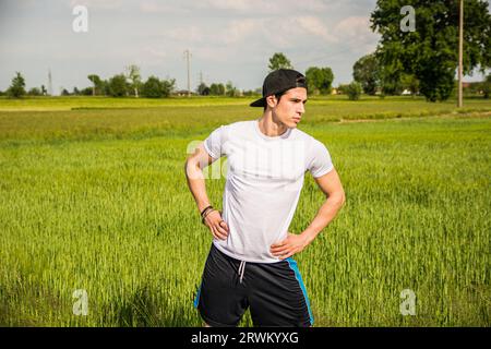 Ein Mann, der auf einem Feld steht, mit den Händen auf der Hüfte. Foto eines jungen Athleten, der mit den Händen auf der Hüfte selbstbewusst auf einem Feld steht Stockfoto
