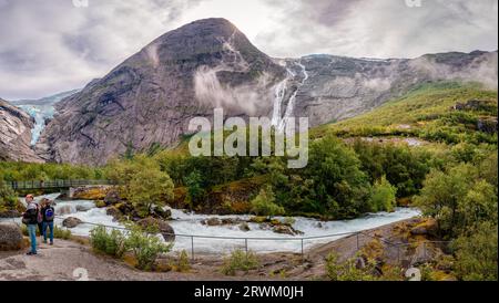 Briksdalen, Norwegen - August 22 2022: Der Fluss Briksdalselva mit der Fußgängerbrücke und der Gletscher Briksdalsbreen auf der linken Seite, in der Jostedalsbre Stockfoto