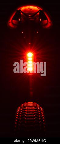 Die leuchtend rote hintere LED-Leuchte eines Mountainbikes beleuchtet die Unterseite des Satteles und die Oberseite des Hinterreifens und hebt das Profilprofil hervor. Stockfoto