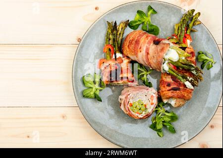 Hackbraten in Speck gewickelt mit Spargel und Frischkäse auf Holztisch. Draufsicht. Leerzeichen für Text. Stockfoto