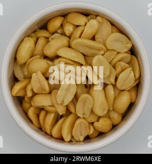 Einige Erdnüsse, die in eine kleine weiße Schüssel für einen Snack gegossen wurden. Stockfoto