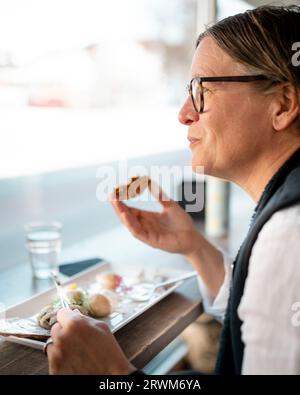 Frau sitzt am Fenster des Restaurants und isst. Stockfoto