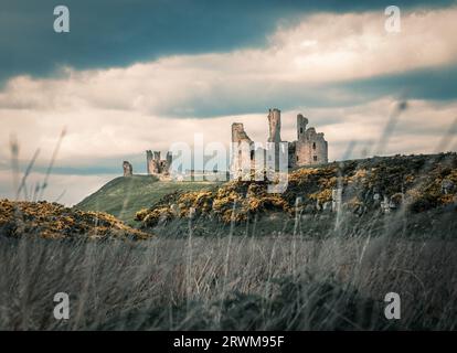 Dunstanburgh Castle Ruinen auf dem Gipfel eines felsigen Hügels mit dramatischem bewölktem Himmel Stockfoto