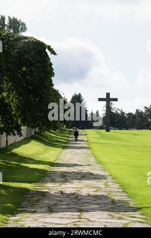 Eine Person auf einem Fahrrad, die entlang einer Straße mit einem Kreuz am Straßenrand fährt Stockfoto