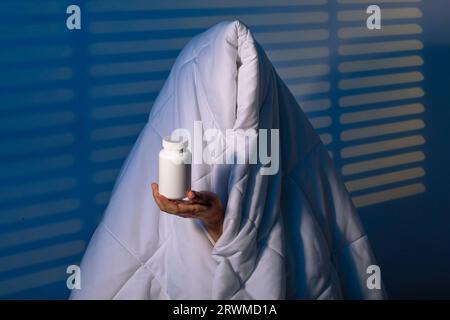 Looking Serenity: Mädchen bekämpft Schlaflosigkeit unter seiner treuen Decke mit Schlafkapsel vor dem Hintergrund der Nachtwache mit Jalousien Stockfoto