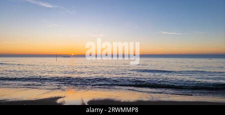 Weiter Blick auf einen farbenfrohen Himmel über der Nordsee, wo die Sonne hinter einem Wolkenufer untergeht Stockfoto