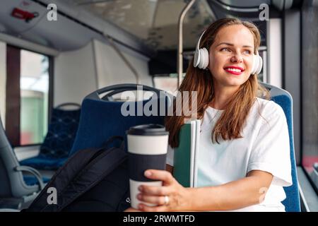 Eine brünette Frau mit rotem Lippenstift und weißem T-Shirt sitzt im City Shuttle Bus und hört Musik mit ihren Kopfhörern. Stockfoto