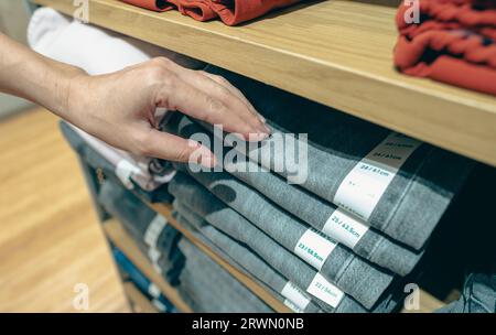 Frauen kaufen Jeans im Bekleidungsgeschäft ein. Eine Frau, die sich Kleidung aussucht. Jeans auf Holzregalen im Bekleidungsgeschäft. Modegeschäft im Einkaufszentrum. Stockfoto