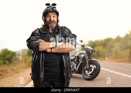 Reifer bärtiger Biker mit Helm und Lederjacke, der vor einem Hubschrauber auf der Straße steht Stockfoto