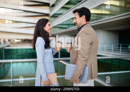 Fröhliche, selbstbewusste Geschäftsleute mittleren Alters trinken Kaffee zum Mitnehmen im Freien Stockfoto