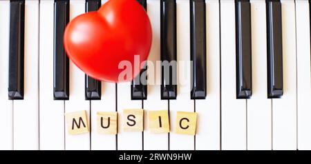 Wortkünstler aus Holzwürfeln auf einem S ynthesizer-Schlüssel auf schwarzem und weißem Hintergrund mit rotem Herzen. Klavieroktave aus nächster Nähe. Keyboard-Musical i Stockfoto