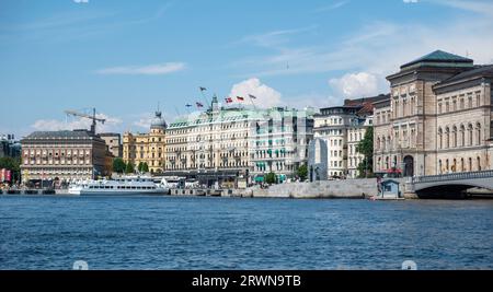 Stockholm, Schweden. Imposantes Gebäude am Ufer des Strandvagen-Ufers im Stadtteil Ostermalm. Vor Anker gelegenes Boot am Hafen, Menschen, blauer Himmel Hintergrund. Stockfoto