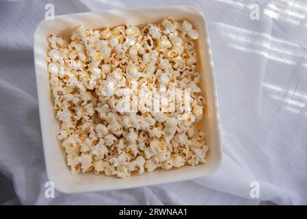 Weißes selbstgemachtes Popcorn in einer weißen Schüssel, Nahaufnahme. Eine Schüssel mit frisch gemahlenem Popcorn Stockfoto