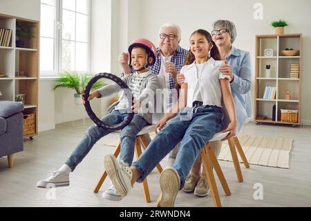Lustige Großeltern und Kinder spielen Spiele, haben Spaß und geben vor, Auto zu fahren Stockfoto
