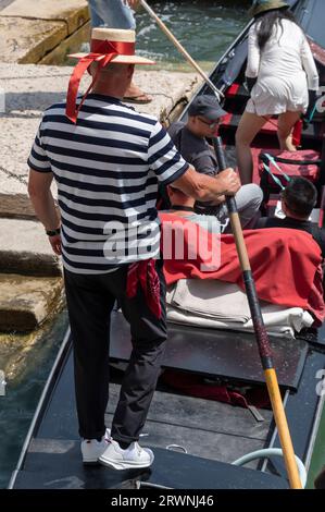 Ein Gondolier mit seinem bekannten schwarz-weiß gestreiften Hemd und Bootsfahrer ist ein Ruderer, der eine Gondel mit einem langen Ruder steuert und Touristen für eine kurze Tour nimmt Stockfoto