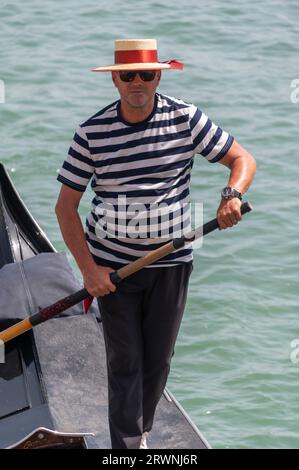 Ein Gondolier mit seinem bekannten schwarz-weiß gestreiften Hemd und Bootsfahrer ist ein Ruderer, der eine Gondel mit einem langen Ruder steuert und Touristen für eine kurze Tour nimmt Stockfoto