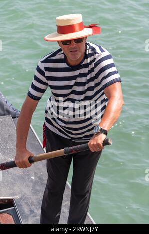 Ein Gondolier mit seinem bekannten schwarz-weiß gestreiften Hemd und Bootsfahrer ist ein Ruderer, der eine Gondel mit einem langen Ruder steuert und Touristen für eine kurze Tour nimmt Stockfoto