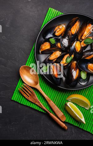 Meeresfrüchte Muscheln und Basilikumblätter in einer schwarzen Platte auf Bambus matte und Tisch aus Stein. Ansicht von oben. Stockfoto