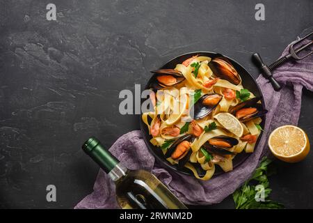 Spaghetti-Vongole, italienische Meeresfrüchte-Pasta mit Muscheln und Muscheln, auf dem Teller mit Kräutern und einem Glas Weißwein auf rustikalem Steinhintergrund. Traditionell I Stockfoto