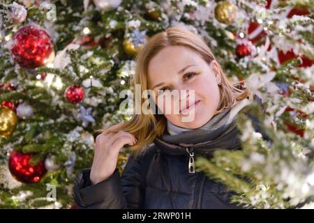Porträt einer schönen lächelnden europäischen Frau auf Weihnachtsbaumhintergrund. Junge glückliche Frau in den Neujahrsferien. Stockfoto