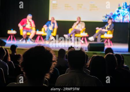 Kollegen, die während der Konferenz auf der Bühne sitzen und Fragen von Zuschauern im dunklen Saal beantworten, während sie ein neues Projekt vorstellen Stockfoto